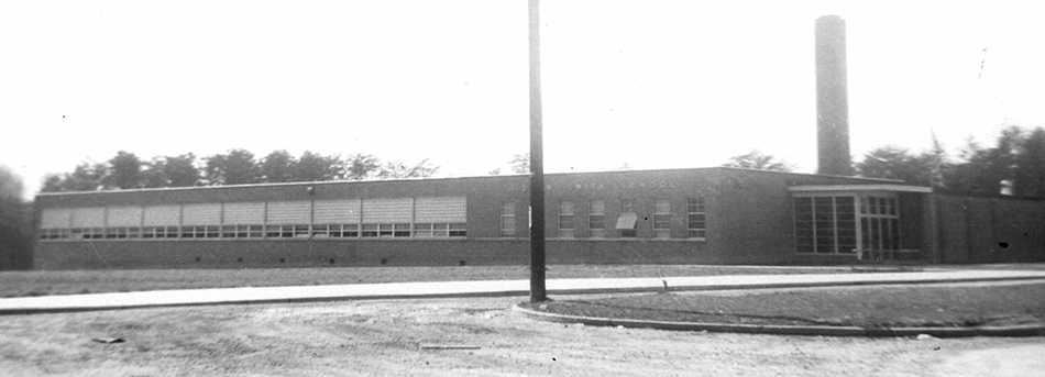 Black and white photograph of Drew-Smith Elementary School taken in 1958 during a fire insurance survey of school properties for the Fairfax County School Board. The building is much smaller than Belle View. It is a single story brick structure with a tall chimney near the main entrance. 